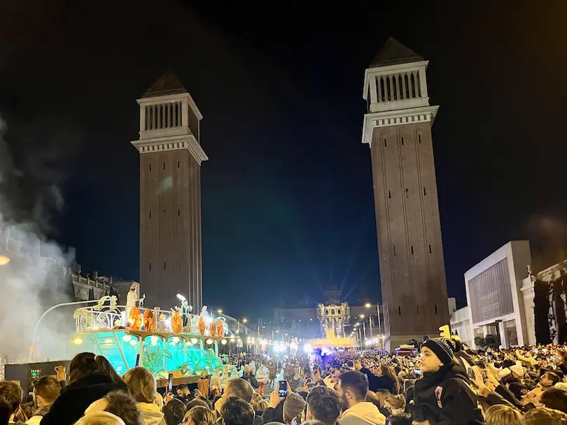 Two Venetian style towers rising in the sky at night. A lot of people have gathered for festivities.