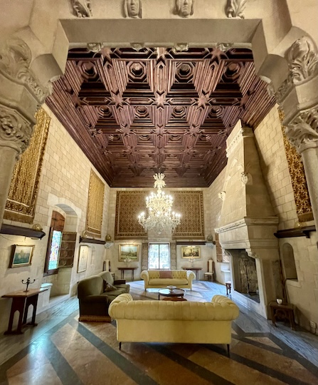 Another room in the castle with a heavy wooden ceiling with sofas in the middle of the room and a massive chandelier hanging in the middle.
