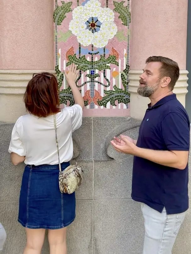 best-gaudi-architecture-tour-the-barcelona-feeling-01 Tour guide Christian on the right is explaining a guest on the left the importance of the mosaics in architecture in Barcelona. The woman touches the mosaic.